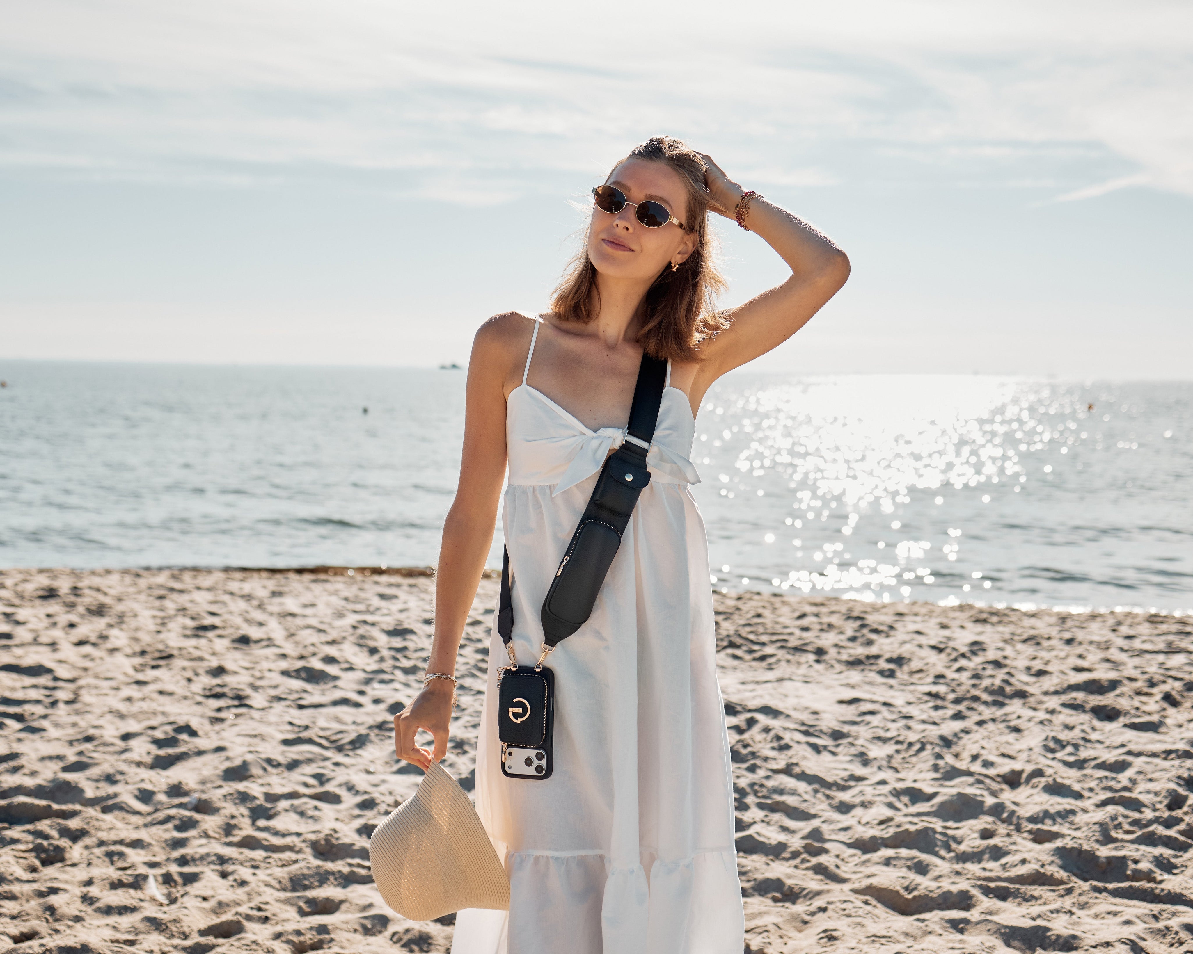 Woman on a sandy beach wearing a Custype black crossbody wallet phone case with strap — hands-free iPhone carry for travel and everyday use