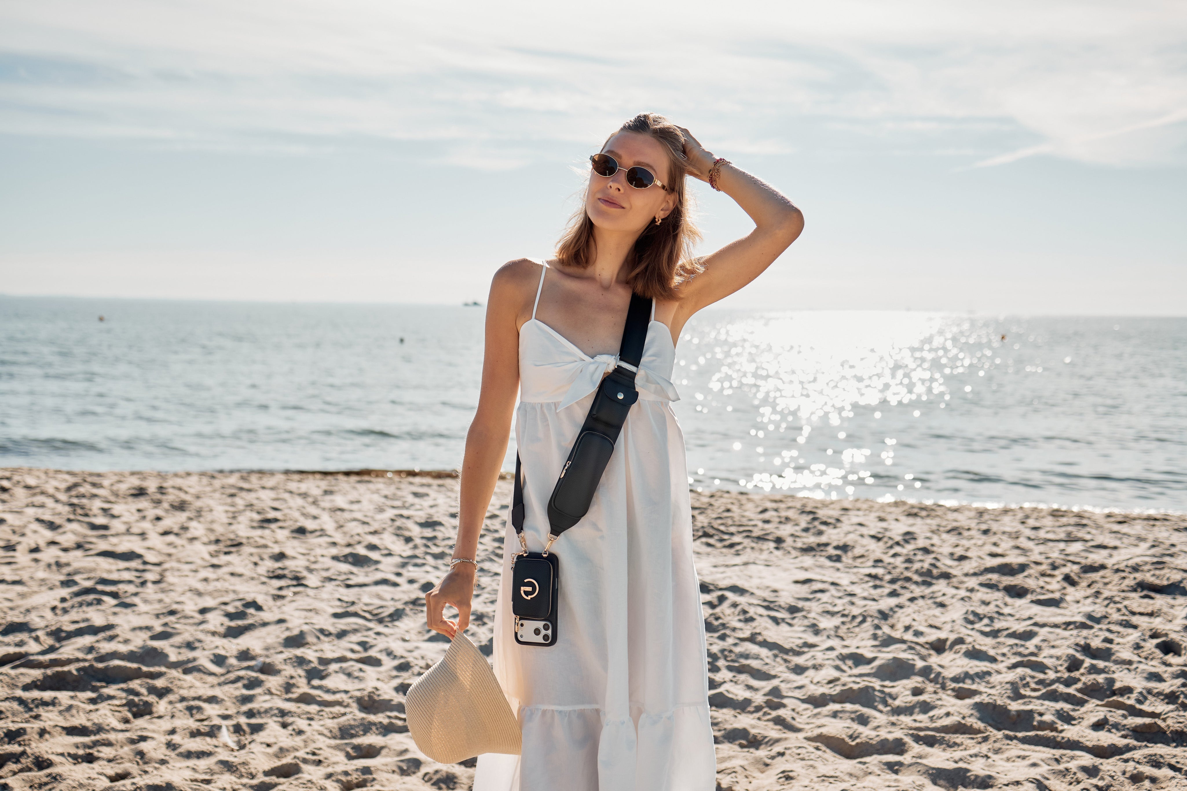Woman on a sandy beach wearing a Custype black crossbody wallet phone case with strap — hands-free iPhone carry for travel and everyday use