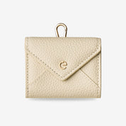 Beige envelope-inspired AirPods pouch with leather finish and detachable gold-tone clip for everyday carry