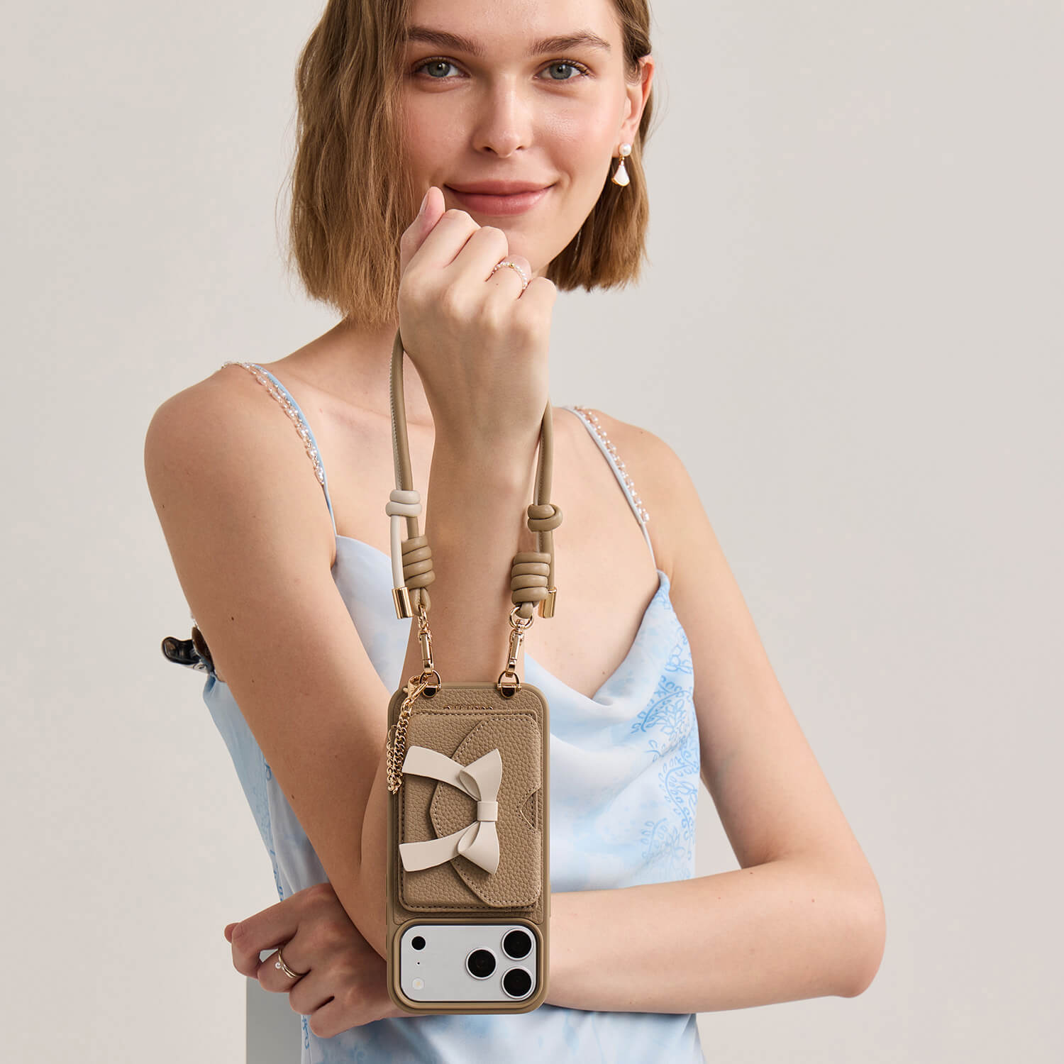 iPhone 18 Pro Max MagSafe wallet case with taupe leather finish, detachable bow wallet, safety chain and stylish wrist strap for everyday outings